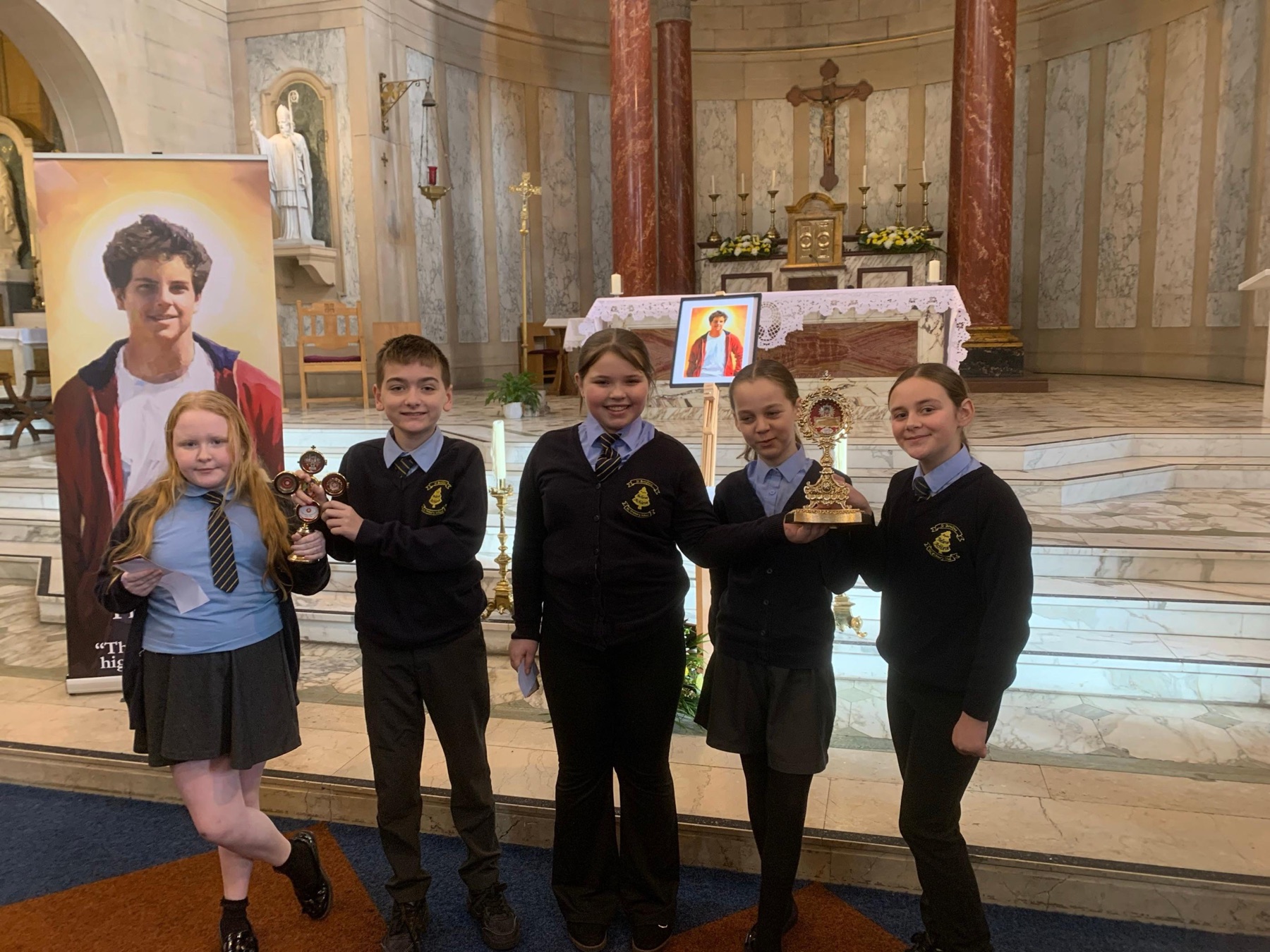 St Boniface pupils in church beside an image of St Carlo Acutis