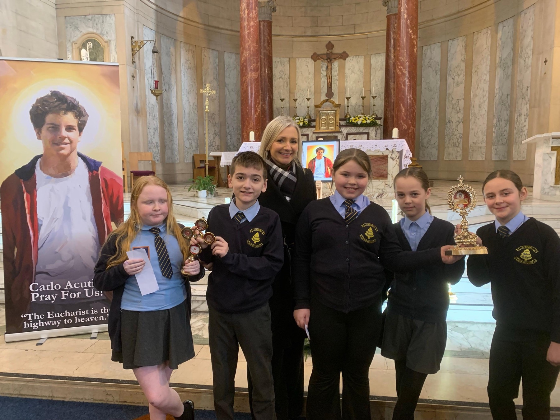 St Boniface pupils and a member of staff in church beside an image of St Carlo Acutis